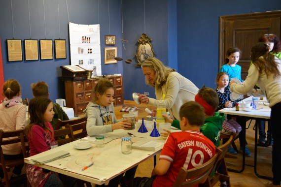 Foto einer Schulklasse in einem Museumsraum bei der Kräuterführung, sie rühren ihr eigenes Fenchelöl an.