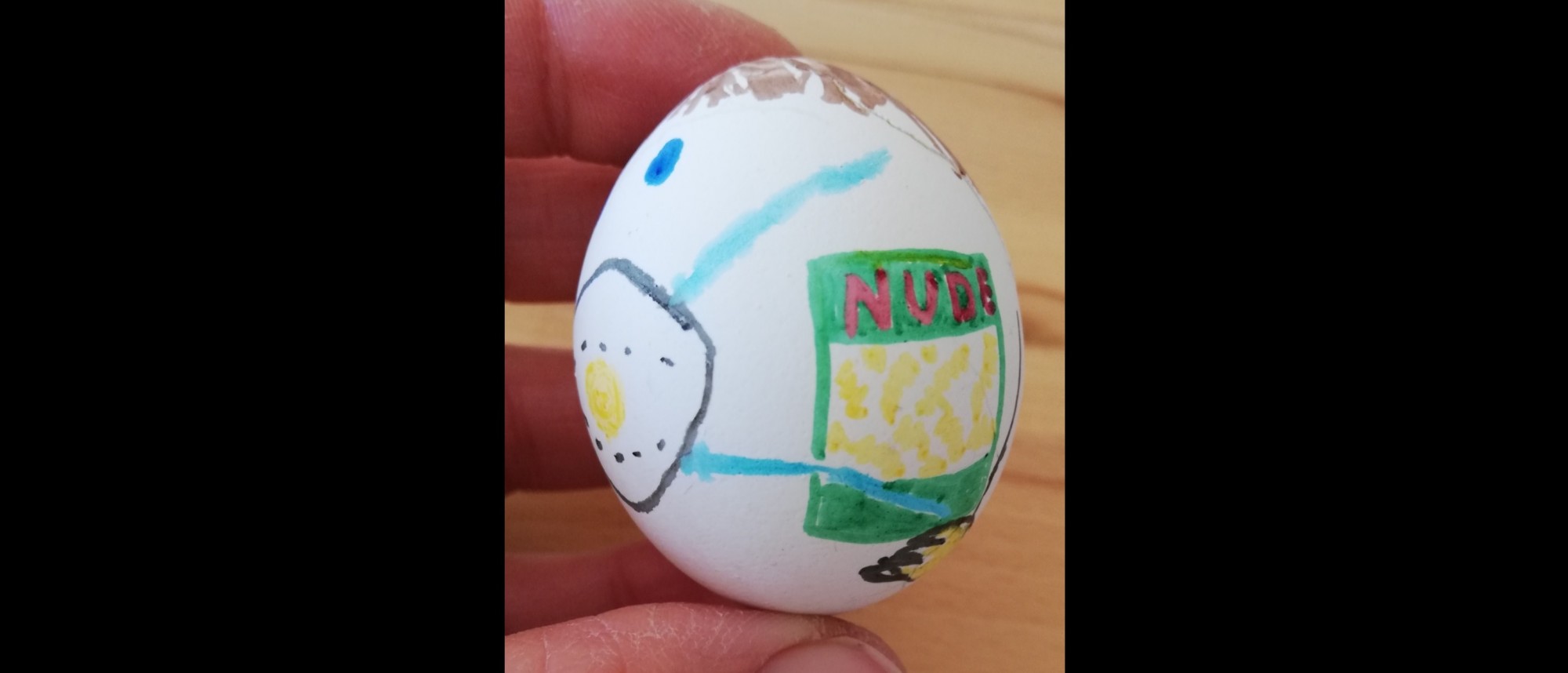 Ein bunt bemaltes Ei, aufgemalt sind eine FFP2-Maske im Gesicht und eine Packung Nudeln.