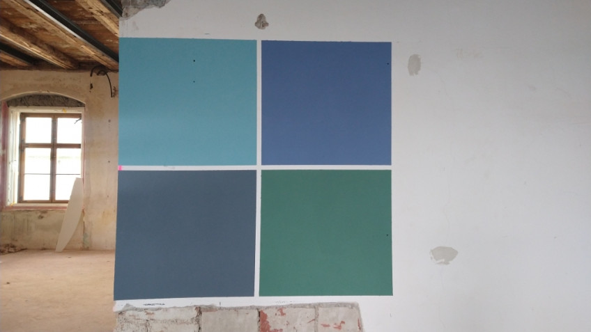 Vier Farbfelder in hellblau, dunkelblau, dunkelgrau und dunkelgrün im Quadrat auf einer weißen Wand angebracht