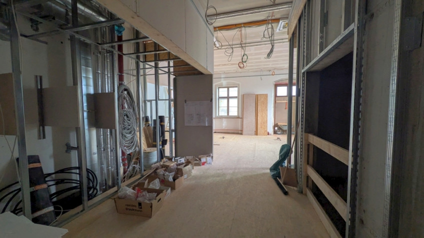 Rechts ein Aufzugsschacht, links gegenüber eine Wand mit Kabeln und Rohren.