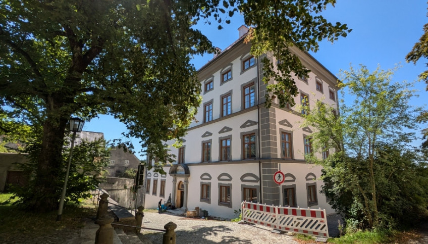 Das Stadtmuseum Landsberg am Lech von Nordost, eingerahmt von Bäumen, am Weg eine Absperrung für Fußgänger