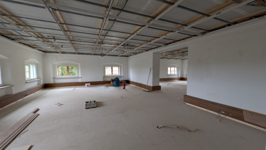 Großer Raum mit tiefhängender Decke und niedrigen Fenstern, Durchgang in einen weiteren Raum