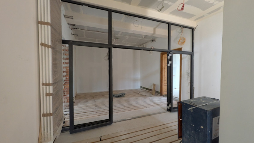 Blick durch eine Glastür auf einen kleinen Raum im Flur, von dem zwei Türen wegführen.