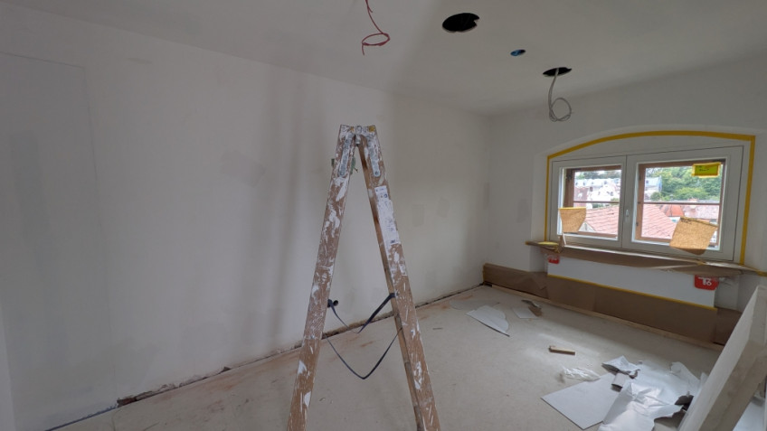 Kleiner Raum mit niedrigem Fenster, in der Mitte steht eine Leiter.