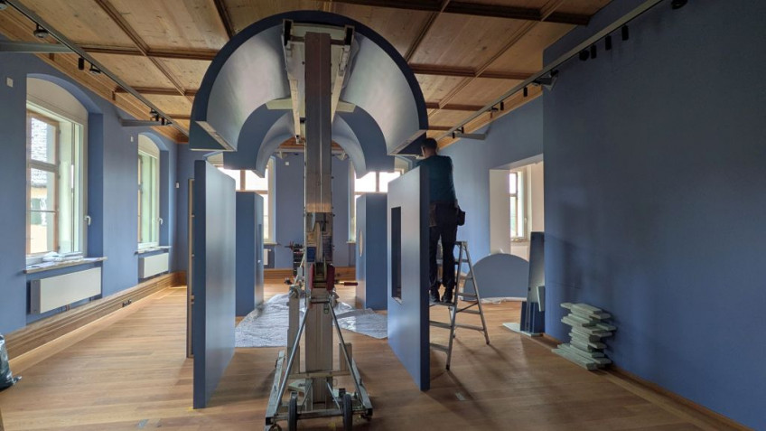 In der Mitte eines Raumes wird mit Haltevorrichtungen ein blauer Gewölbebau aufgebaut.